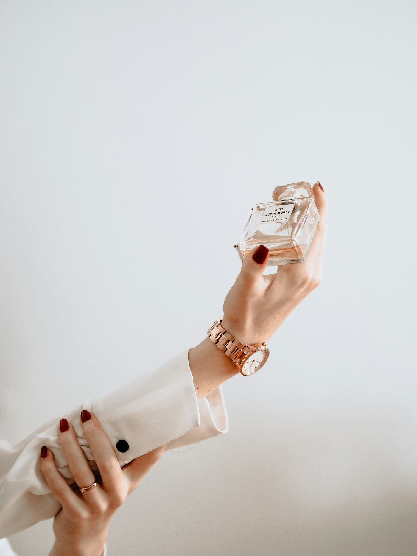Hand holding a small perfume bottle against a pale wall